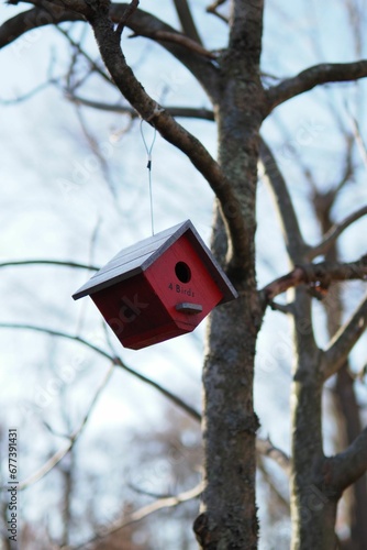 Vertical shot of a dark red birdhouse hanging from a tree branch. © Wirestock