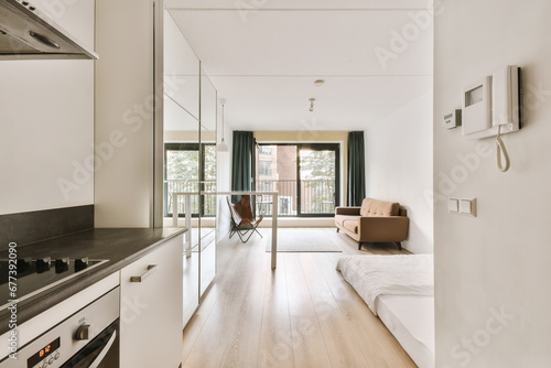 a kitchen and living room in a house with white walls  wood flooring and black countertops on either side