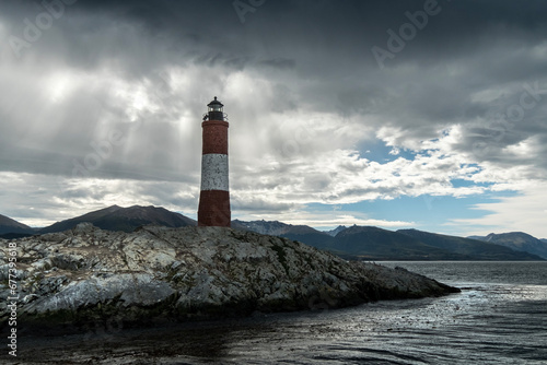 Panoramic view of the rocky island where the Les Eclaireurs lighthouse is located, under a cloudy sky and the mountains in the background. Ushuaia, Tierra del Fuego, Argentina