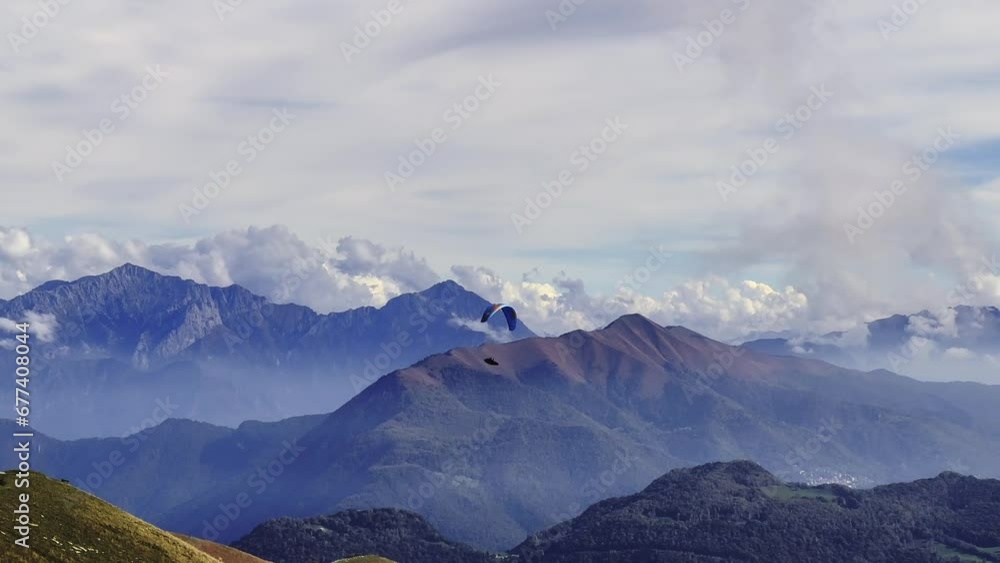 Aerial View over Paraglider Flying over Beautiful Cloudscape and Mountainscape with Sunlight in a Sunny Day in Ticino, Switzerland, Europe Aerial View over Paraglider Flying over Beautiful Cloudscape and Mountainscape with Sunlight in a Sunny Day in Ticino, Switzerland, Europe