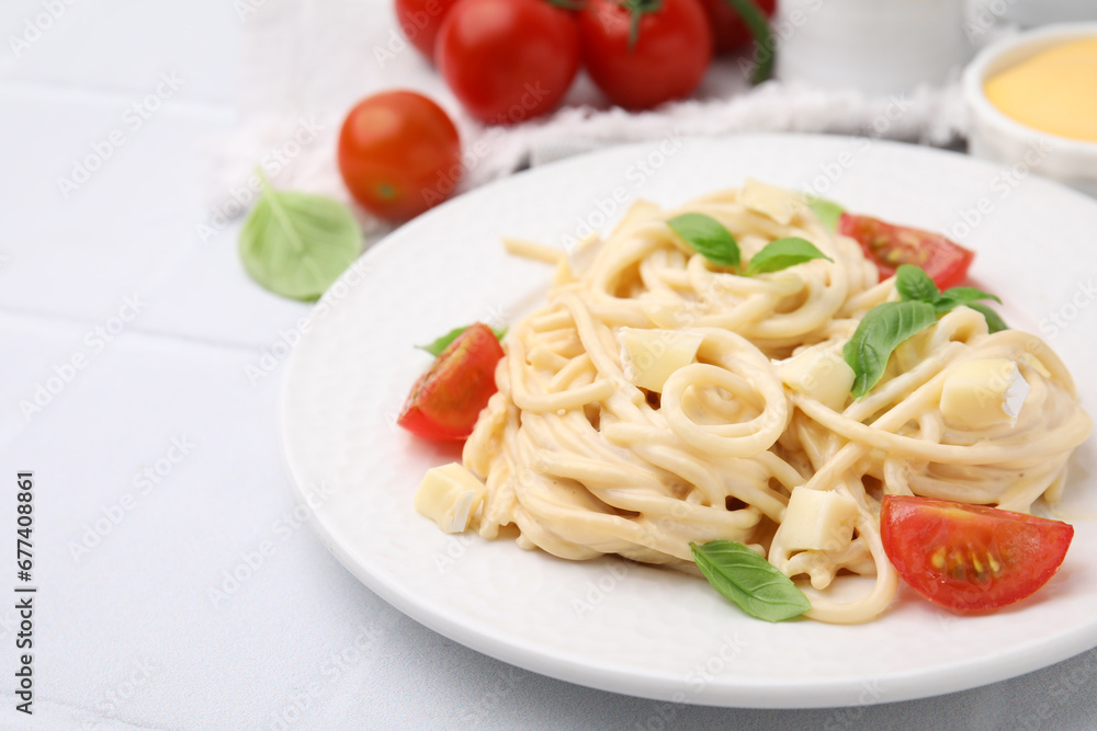 Delicious pasta with brie cheese, tomatoes and basil leaves on white tiled table, closeup. Space for text