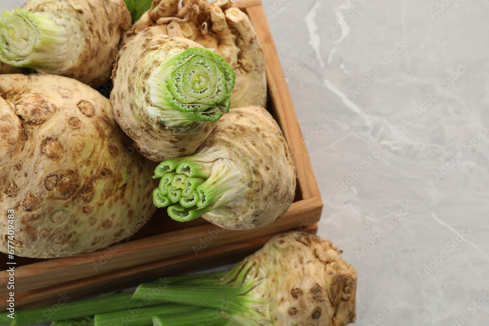 Fototapeta premium Fresh raw celery roots and wooden crate on light grey table, above view. Space for text