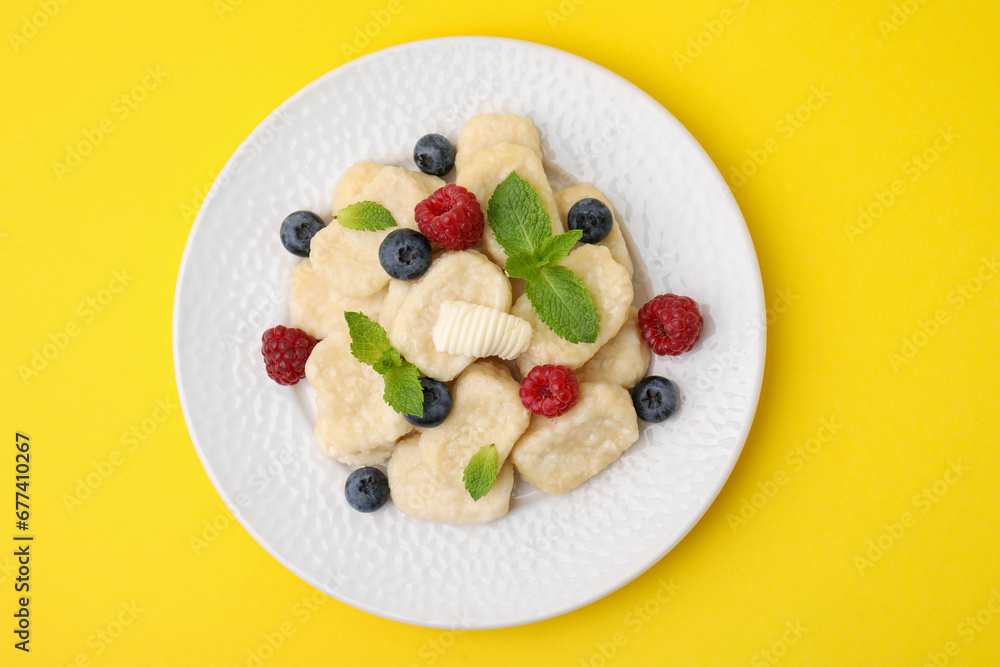 Plate of tasty lazy dumplings with berries, butter and mint leaves on yellow background, top view