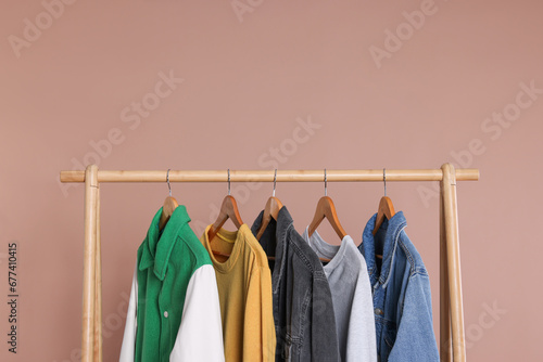 Rack with stylish clothes on wooden hangers against beige background