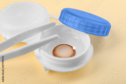 Case with color contact lenses and tweezers on pale yellow background, closeup
