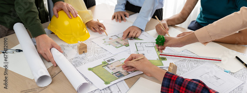 Professional architect cooperate with engineer discussing the use of green design in eco house project on table with blueprint and architectural equipment scatter around. Closeup. Delineation.