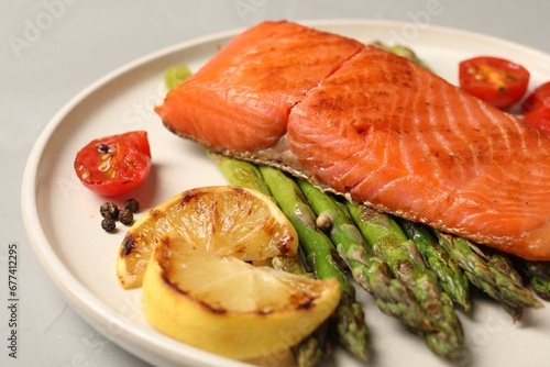 Tasty grilled salmon with asparagus, tomatoes, spices and lemon on light grey table, closeup