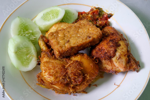Close up Fried chicken, fried tempeh, cucumber and sambal served on the plate.