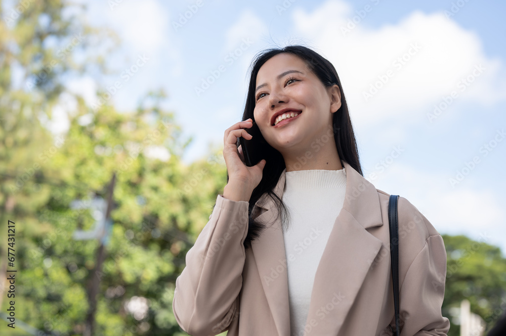 A beautiful Asian businesswoman is talking on the phone while walking in the city. Urban city life A beautiful Asian businesswoman is talking on the phone while walking in the city. Urban city life