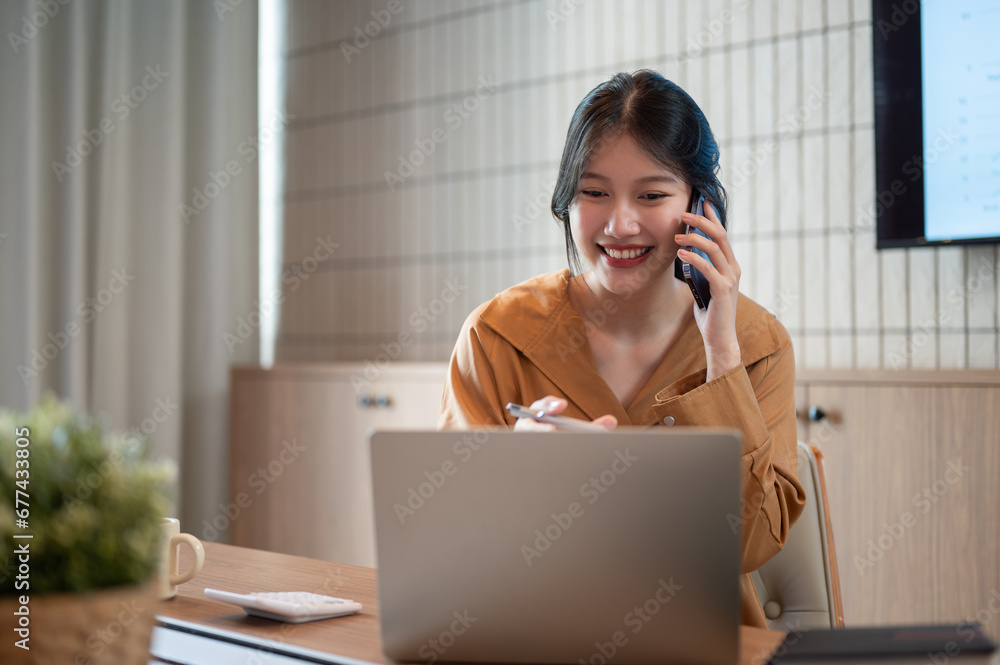 A beautiful Asian businesswoman is talking on the phone with her client while working in her office. A beautiful Asian businesswoman is talking on the phone with her client while working in her office.