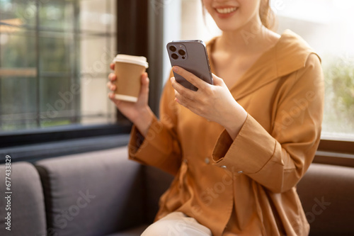 A beautiful Asian woman is enjoying her coffee and using her smartphone while relaxing in a cafe.