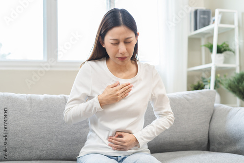 Acid reflux disease, suffer asian young woman have symptom gastroesophageal, esophageal, stomach ache and heartburn pain hand on chest from digestion problem after eat food, Healthcare medical concept photo