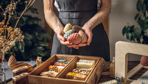 A woman soap maker holds soap in her hands in the form of colorful coniferous cones. A lot of different sliced pieces in a wooden box. Eco-friendly natural handmade cosmetics photo