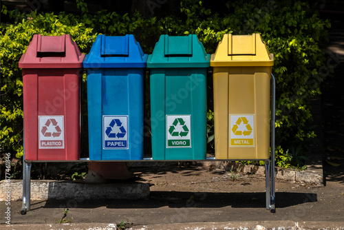 Four color trash cans for recycling, with the words Plastic, Paper, Glass and Metal in Portuguese on the park in Brazil