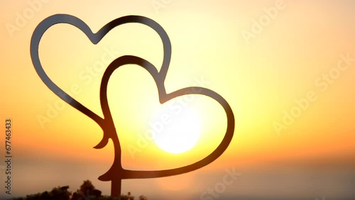 Two black outlines of heart at dawn and sunset on sky on seashore. Stick contours in shape of heart in sand on backdrop of setting and rising sun on seashore. Concept Love infatuation Valentine's Day photo