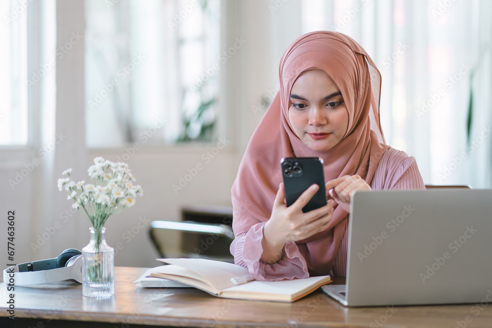 Asian muslim business woman wearing hijab using phone while working at computer in office. Asian muslim business woman wearing hijab using phone while working at computer in office.