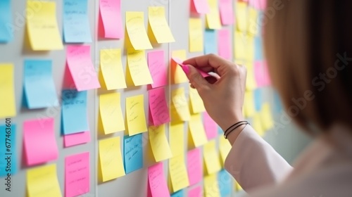 Woman organizer attaches colorful sticky notes to white board. Life hack for easy memorization and reminders of important things in visible place in office. Organization of space and clear schedule