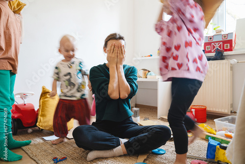 Stressed out mother sitting on floor while children running around her. photo
