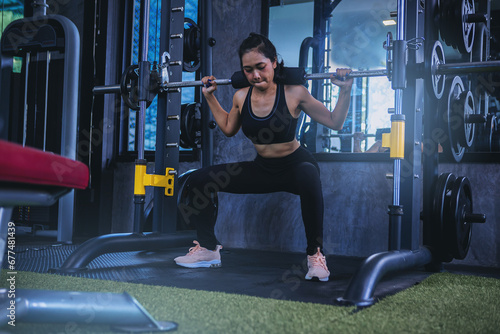 Fit young woman holding her hands with a weight barbell for pulling, squatting, workout in the fitness gym.