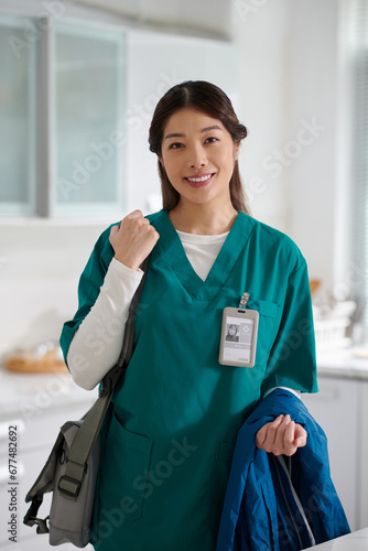 Portrait of smiling medical nurse with bag and jacket standing in kitchen