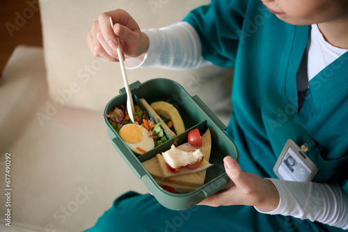 Medical nurse with lunchbox eating salad and sandwiches in hospital lounge area photo