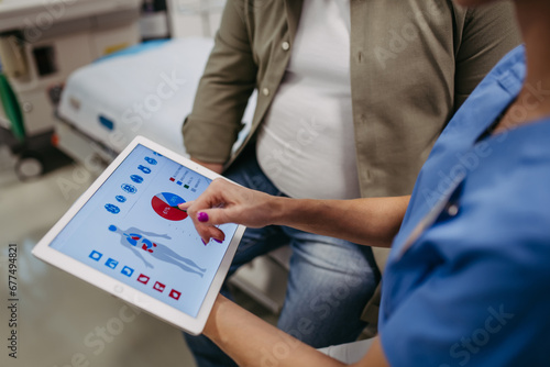 Close up of female doctor consulting with overweight patient, discussing test result in doctor office. Showing medical report on tablet. Obesity affecting middle-aged men's health. Concept of health photo