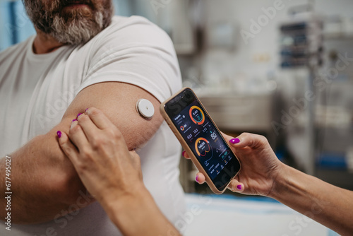Doctor connecting continuous glucose monitor with smartphone, to check blood sugar level in real time. Obese, overweight man is at risk of developing type 2 diabetes. Concept of health risks of photo