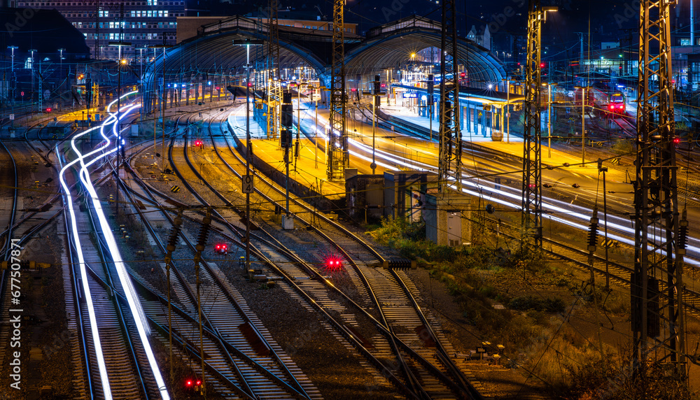 Station with railway tracks, platforms, hall, signals and light traces of passing passenger trains in Hagen, Germany. Colorful early morning twilight atmosphere with longtime exposure from bridge.