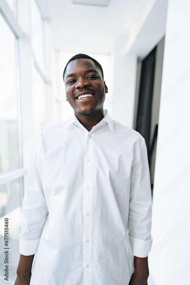 Young african man in white shirt and glasses posing near large window Young african man in white shirt and glasses posing near large window