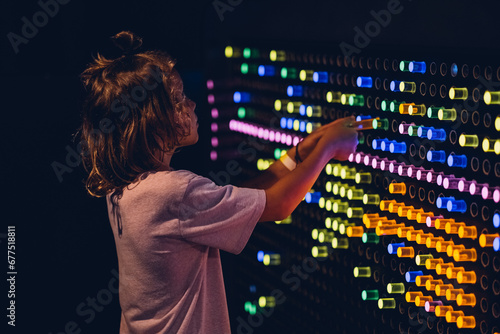 Cute kid boy studying the refraction of light. Child playing with colors flasks in dark room of science museum for children.