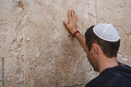 Hand of praying man on the Western Wall in Jerusalem. Tourist in a pile on his head holding the wall crying photo