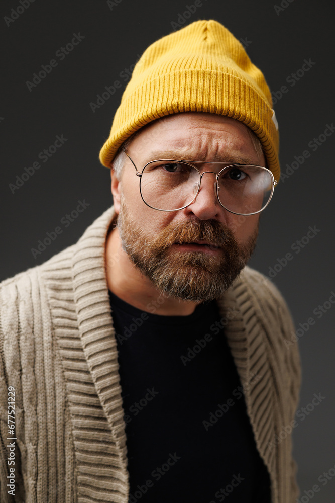 Serious adult man in stylish hat, eyeglasses and knitted cardigan looking at camera isolated on grey Serious adult man in stylish hat, eyeglasses and knitted cardigan looking at camera isolated on grey