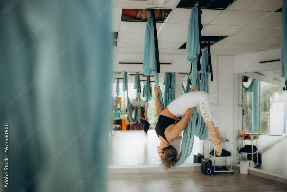 Young pretty slim body fitness girl practicing fly yoga in the gym - obrazy, fototapety, plakaty 