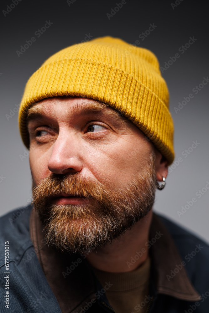 Portrait of trendy bearded man in yellow hat and outwear jacket isolated on grey, menswear concept Portrait of trendy bearded man in yellow hat and outwear jacket isolated on grey, menswear concept