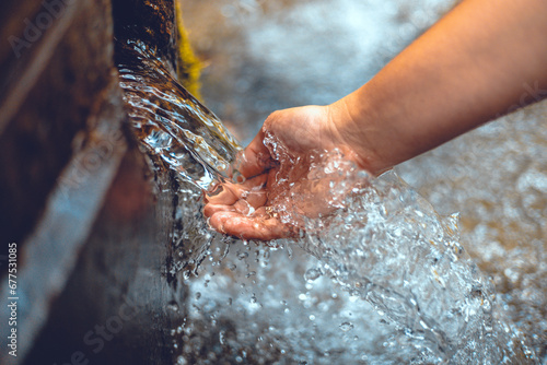 Beautiful photo of a hand under a stream of clear spring water. The woman lowered her hand to touch the stream of clean spring water. The hand touches the cool stream of water. photo