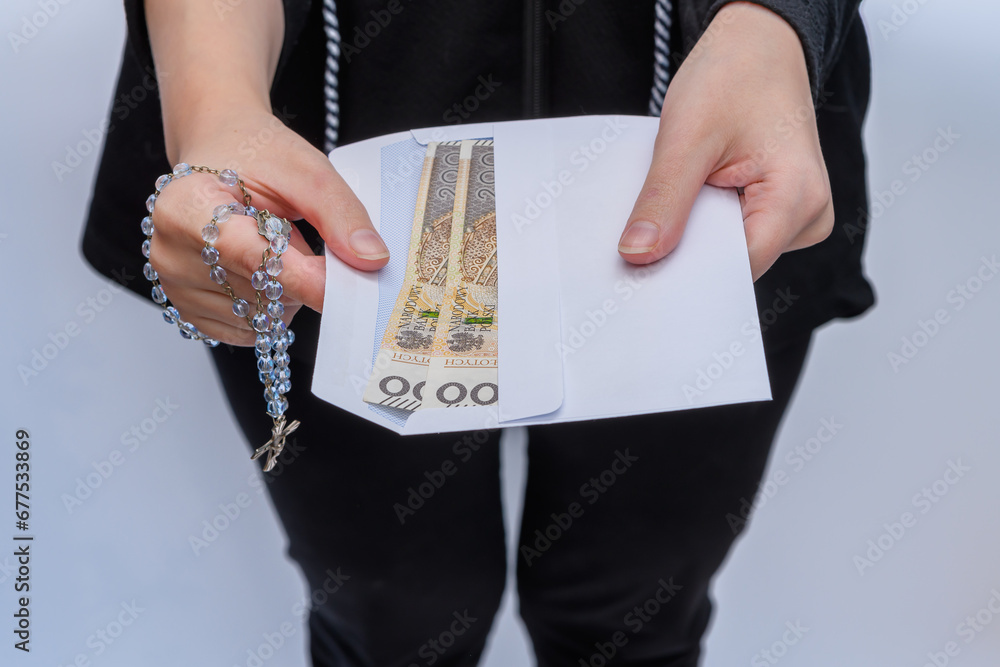 Kobieta trzyma w rękach kopertę z polskimi pieniędzmi i różaniec  - obrazy, fototapety, plakaty 