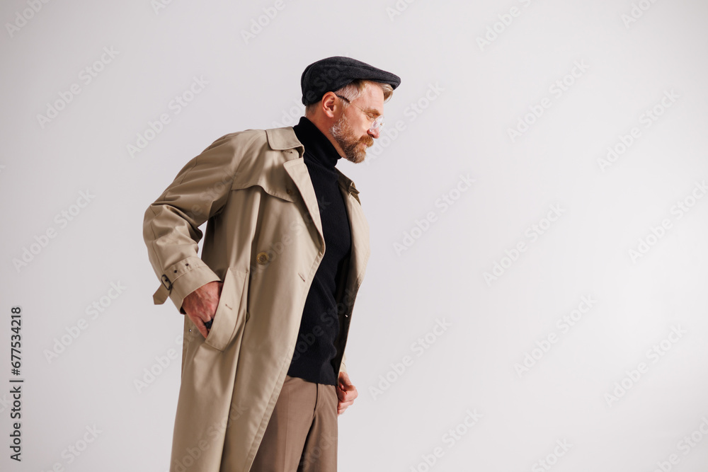 Profile of fashionable blonde man in trench coat and flat cap standing isolated on grey Profile of fashionable blonde man in trench coat and flat cap standing isolated on grey