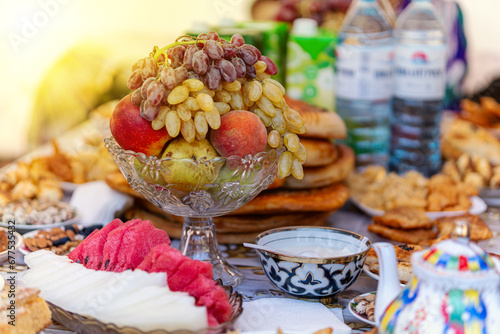 traditional Uzbek dessert - bunch of green grapes ladies fingers , slices of watermelon with bread. Bowl national pattern - Cotton material ikat on wooden background photo