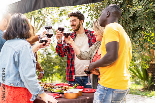 A vibrant outdoor gathering with diverse friends toasting with wine glasses, celebrating a joyful occasion with a barbecue in the background.