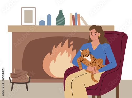 Young woman with a fluffy cat on her lap sitting in armchair near the fireplace. Cat lover.  Warm in winter. Heating system. Energy crises.