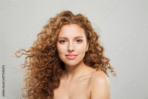 Smiling stylish young female model with curly long brown hairstyle on white background. Woman with wavy hair
