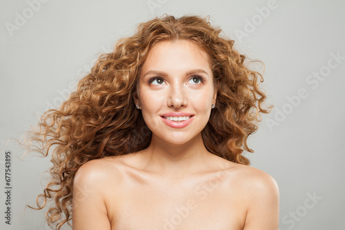 Lovely happy woman with long natural healthy brown curly hair and cute smile looking up on white background. Hair care, hair treatment, wellness and cosmetology concept