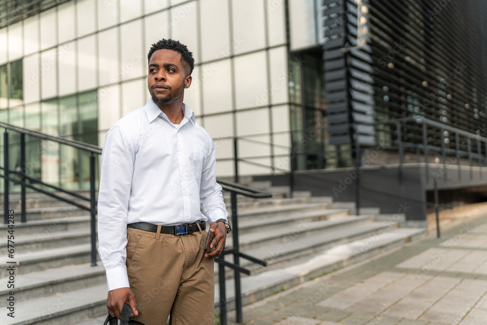 With purpose in his stride, the stylish African-American businessman carries his laptop bag and holds his phone, ready to conquer the day's challenges. With purpose in his stride, the stylish African-American businessman carries his laptop bag and holds his phone, ready to conquer the day's challenges.