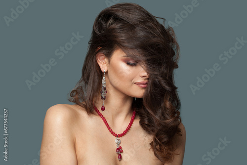Glamorous jewelry model. Beautiful woman with luxurious necklace beads and earring posing on blue background