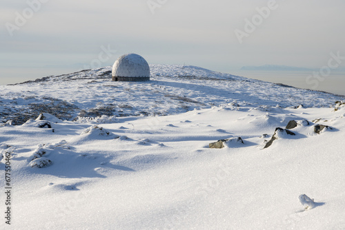 The white dome of an abandoned radar station on the top of a mountain. In the distance, small figures of people on a snow-covered mountain slope. Tourist attraction in the vicinity of Magadan. Russia. © Andrei Stepanov