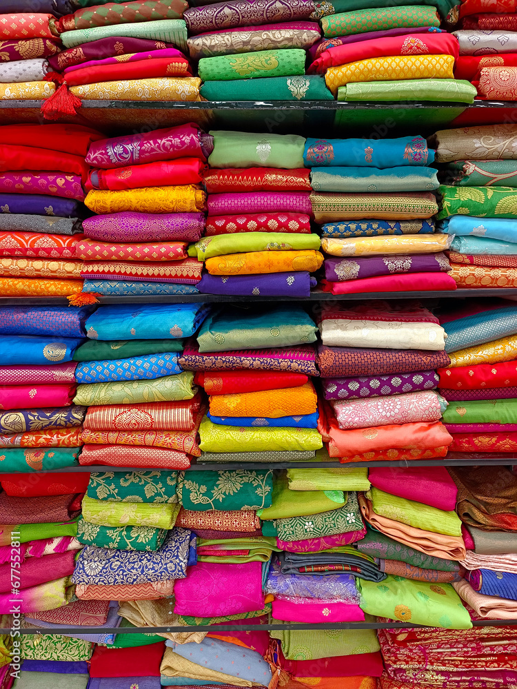 Neatly stacked colorful silk saris in racks in a textile shop, These exquisite, expensive sarees are famous for their gold and silver zari, brocade. Incredible India.