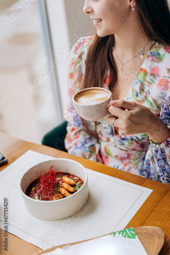 Young beautiful stylish woman drinking coffee while sitting in restaurant and eating tasty dish