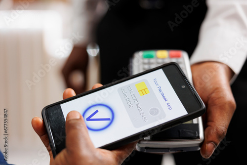 Close up of human hand holding smartphone using mobile nfc payment while paying for hotel services, contactless POS payment. People using banking app to pay via NFC technology, mobile wallet photo