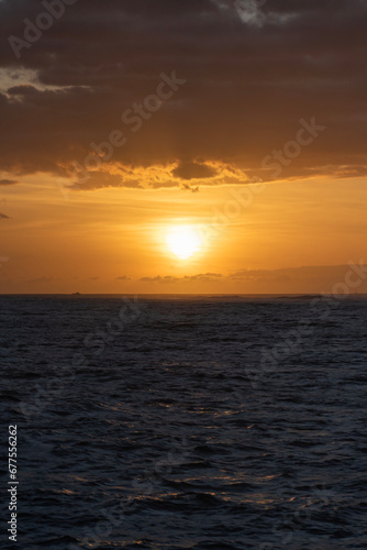 A dramatic orange sunset with colorful clouds and dark blue water from a boat on the Pacific Ocean off of the Island of Kauai in Hawaii  United States. 