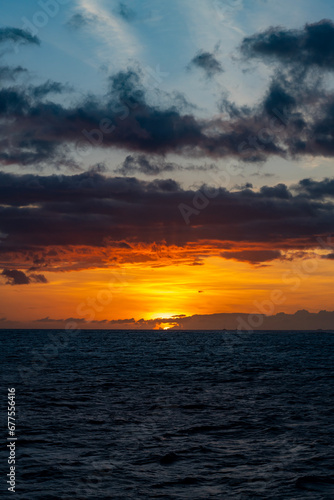 A dramatic orange sunset with colorful clouds and dark blue water from a boat on the Pacific Ocean off of the Island of Kauai in Hawaii  United States. 